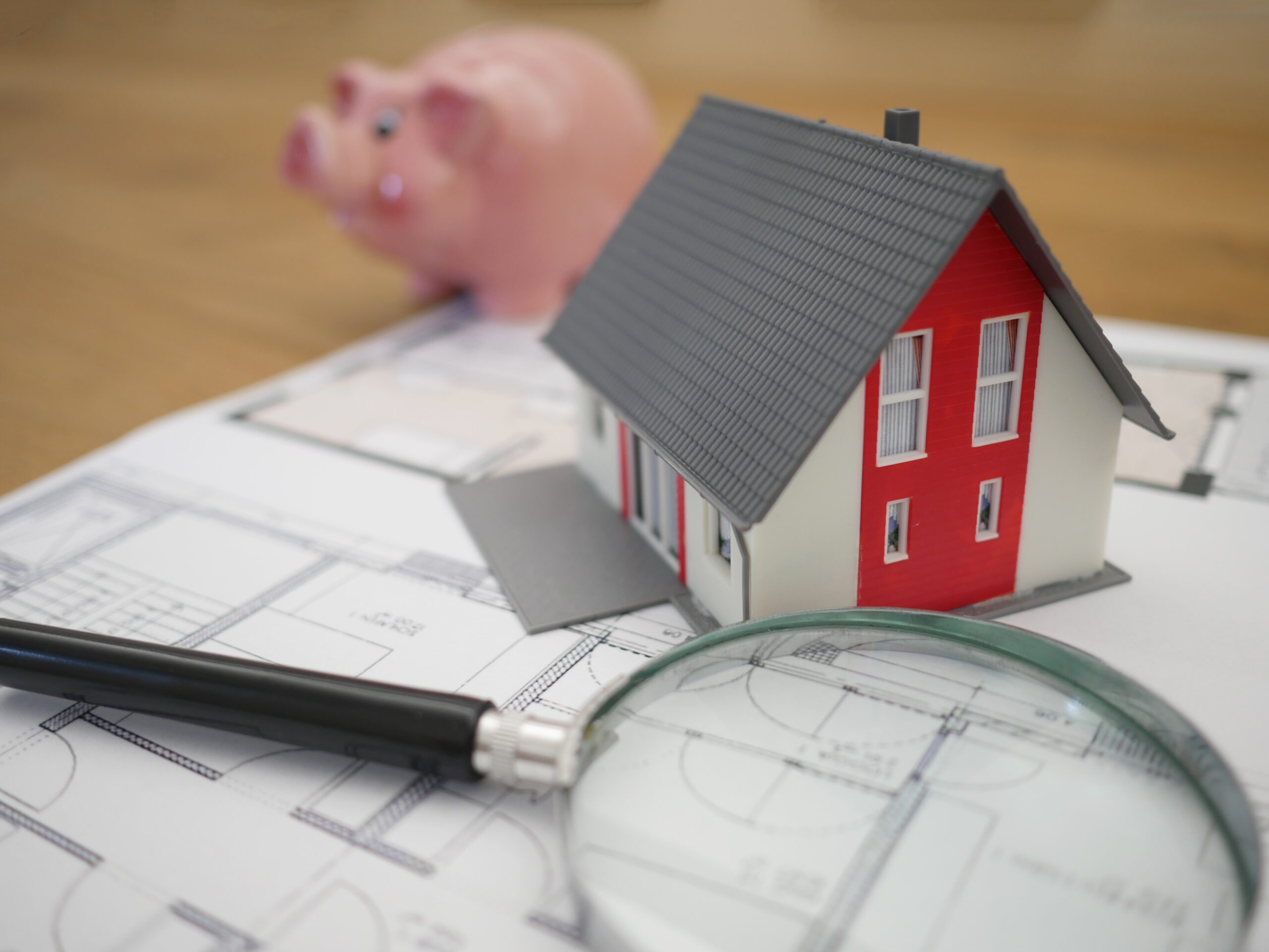 Planung eines neuen Hauses. Im Hintergrund ein Sparschwein, welches auf das Einsparpotential durch neue Investitionen heinweist.